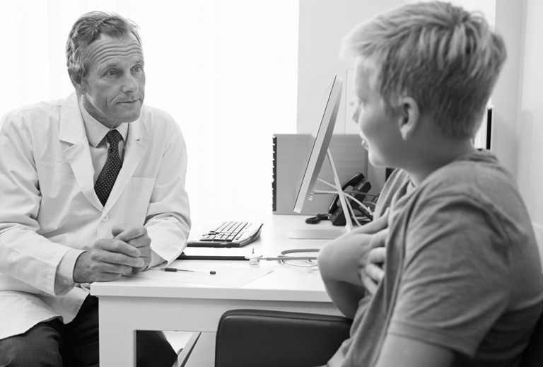 Black and white photo of a health care professional speaking with a young patient.