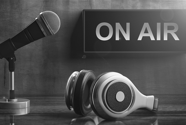 Black and white photo of a microphone and headphones and sign that says on air